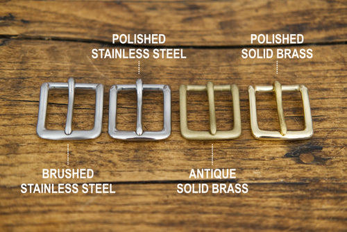 Four metal buckles labeled 'Polished Stainless Steel', 'Polished Solid Brass', 'Brushed Stainless Steel', and 'Antique Solid Brass' on a wooden surface.